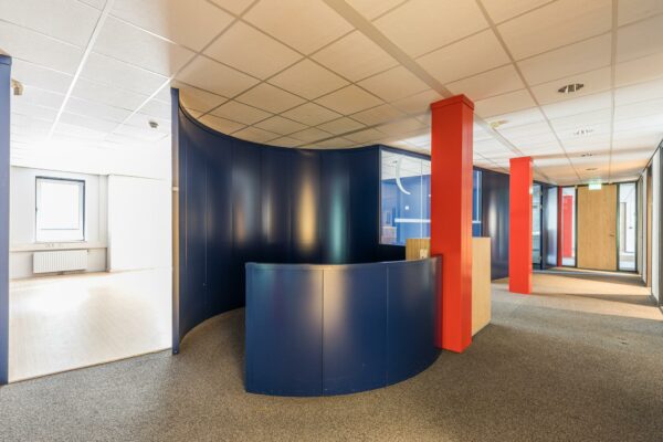 Moderne kantoorruimte aan de Laan Blussé van Oud-Alblas met blauwe ronde balie, rode pilaren en systeemplafond.